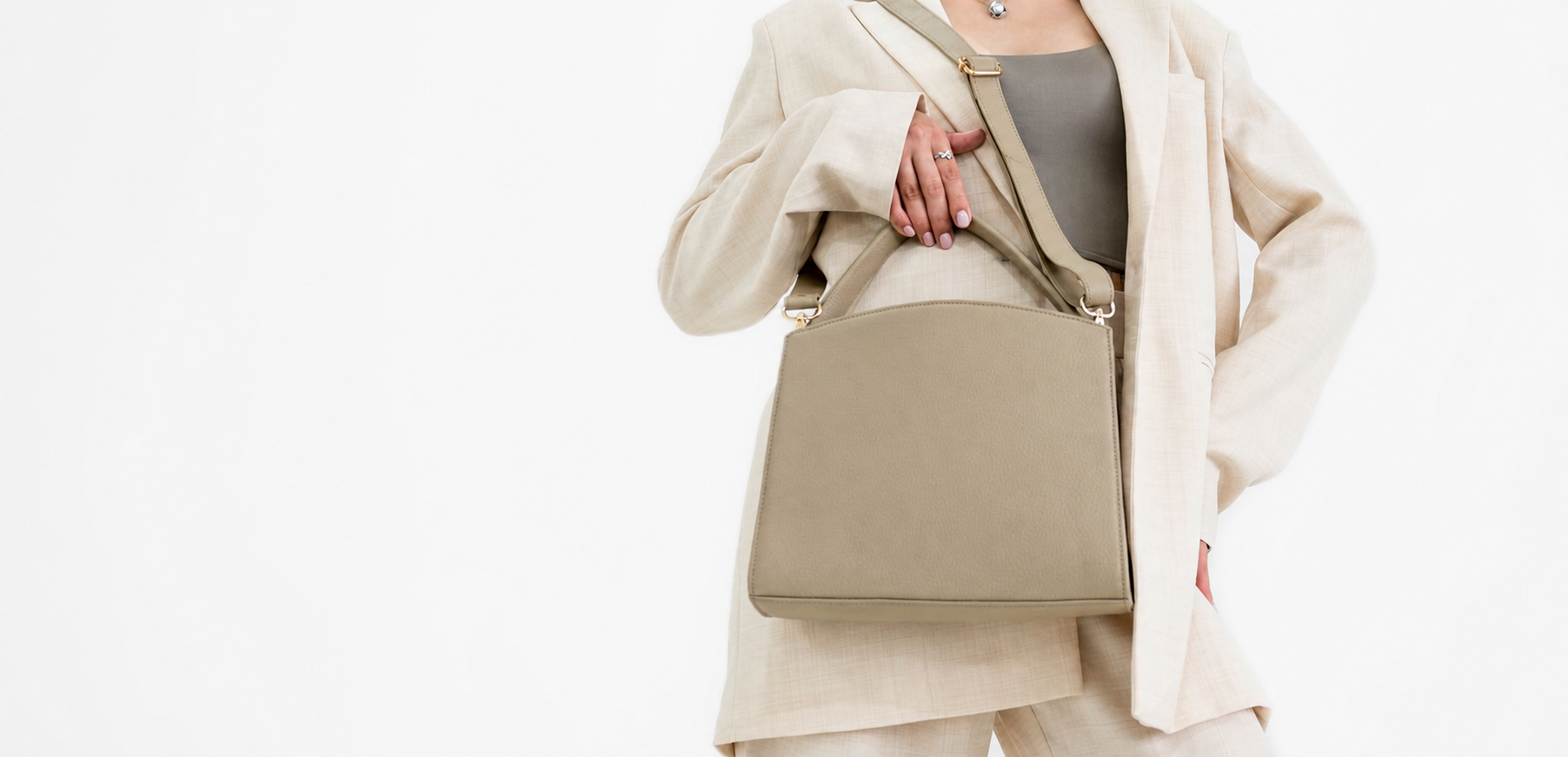 Woman in a neutral suit styling an unbranded structured handbag, cropped below the face